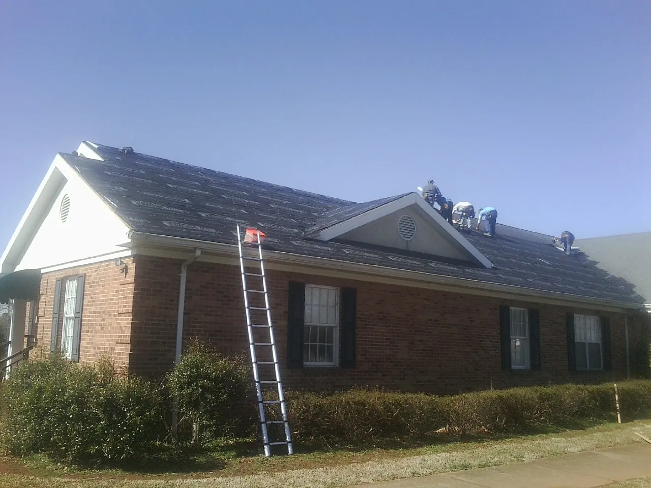 Crew tearing shingles off a brick ranch roof with a ladder set — Emergency Roof Repair work by our crew in Elco