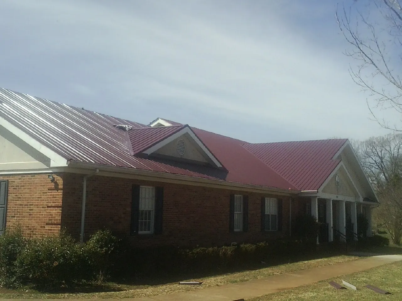 Red metal roof with gabled entries on a long brick building, from a Hail Damage Roof Repair job in Elco