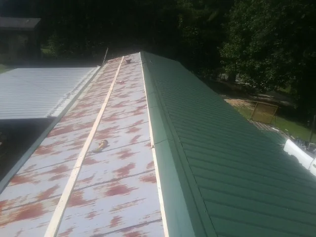 Old rusted panels beside newly installed green metal roofing — Wind Damage Roof Repair by Roofing Brothers in Elco
