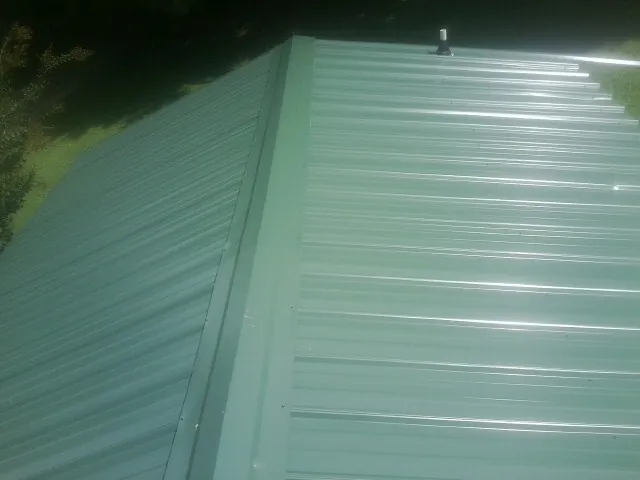 New green metal panels meeting at the ridge of a roof — Flat Roof Repair work by our crew in Elco