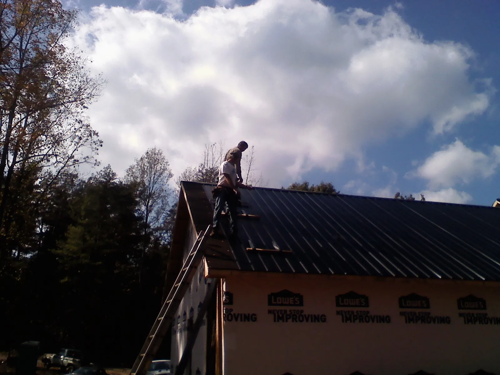Roofer fastening dark metal panels high against a cloudy sky, from a Roof Inspection job in Elco