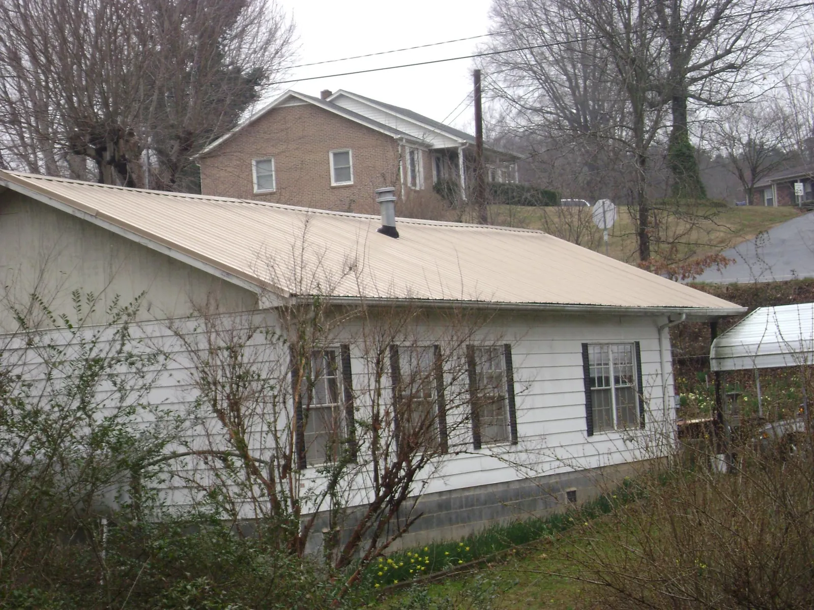 Tan metal roof on a white sided house set into a hillside — Commercial Roofing by Roofing Brothers in Elco