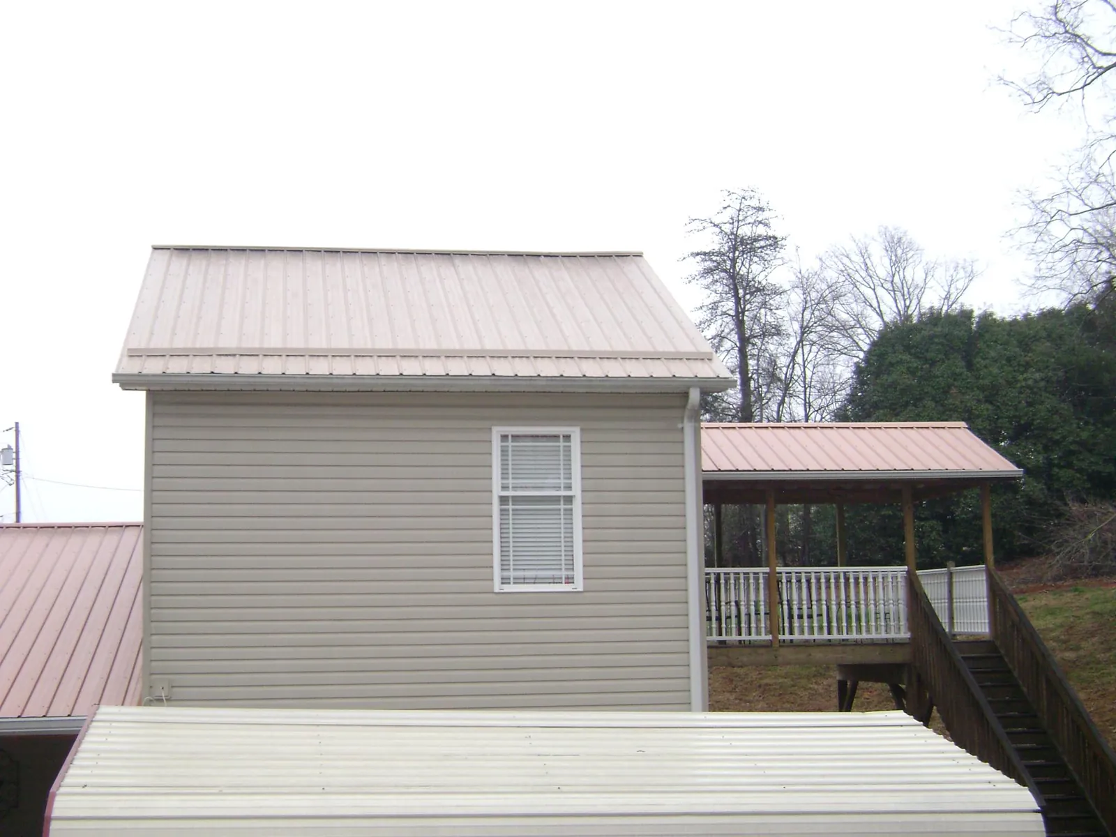 Tan metal roofs on a two story addition and attached porch, from a Roof Replacement job in Elco